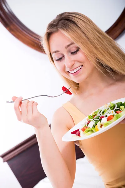 Frau liegt im Bett und isst Salat — Stockfoto