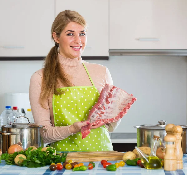 Feliz chica rubia cocinando costillas en casa —  Fotos de Stock