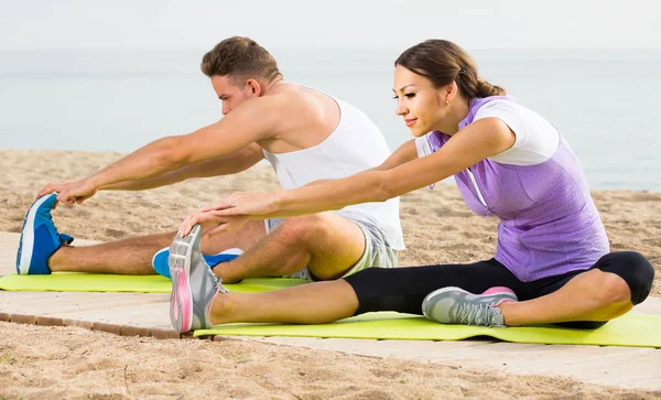 Chico y chica practicando yoga posa sentado en la playa por mar en da — Foto de Stock