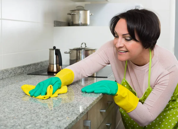 Middle aged female dusting kitchen top — Stock Photo, Image