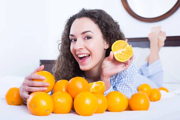 Menina positiva comer laranjas na cama — Fotografia de Stock