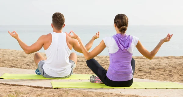 Cross-legged couple practice yoga on beach in morning