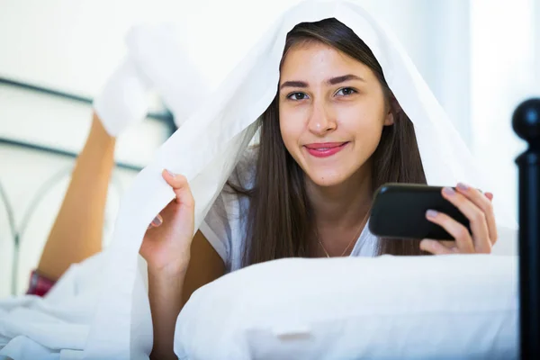 Tonåring Kvinna Gömmer Sig Filt Med Mobiltelefon Och Leende — Stockfoto