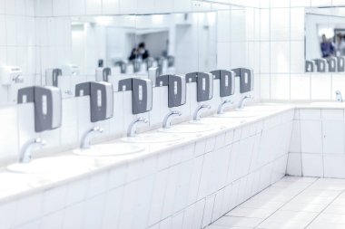 Beyaz parlak gri sabun sahipleri ile musluklar ve umumi tuvalet arka planda siyah sesi içinde aynalar