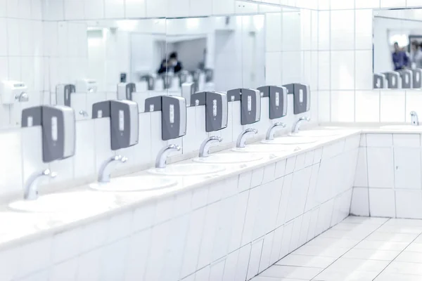 Beyaz parlak gri sabun sahipleri ile musluklar ve umumi tuvalet arka planda siyah sesi içinde aynalar