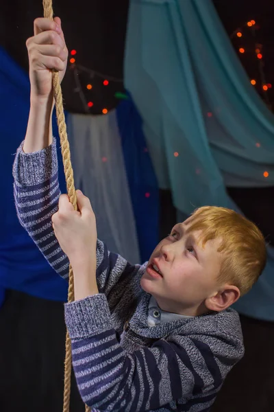 The boy pulls himself up on the rope