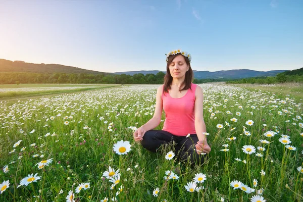 Menina medita em pose de lótus no prado de camomila verde . — Fotografia de Stock