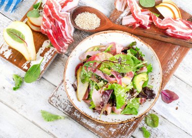 Beyaz ahşap bir masa üzerinde pastırma ile taze karışık salata. 