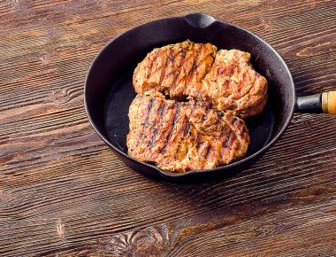 Koyu ahşap bir masa üzerinde tavada kızarmış biftek. 