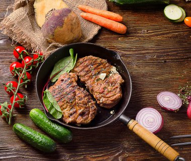 Koyu ahşap bir masa üzerinde tavada kızarmış biftek. 