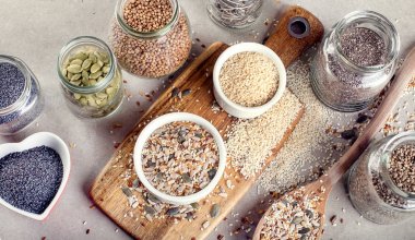 Beyaz kase, ahşap kesme tahtası, vejetaryen ve vegan gıda kavanoz gri arka plan üzerinde farklı tohumların Üstten Görünüm