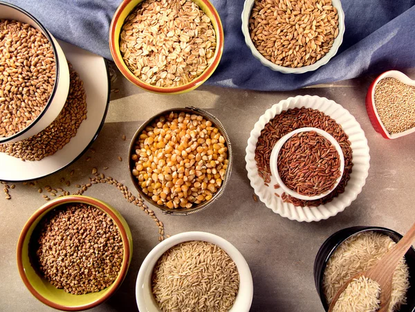 Top view of different healthy grains in ceramic ware on wooden background.