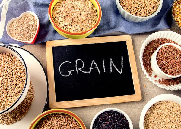 Top view of different healthy grains in ceramic ware, black sign of identification in wooden frame on wooden background.