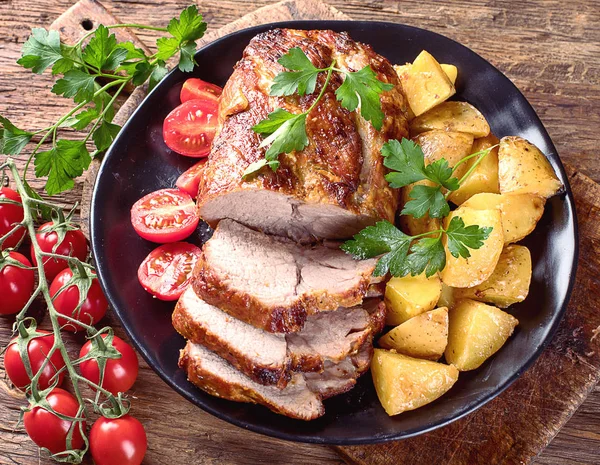 Roast pork with herbs and vegetables on rustic wooden table.