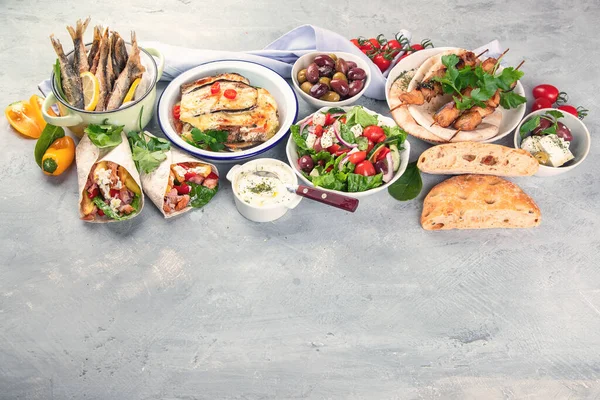 Greek food on grey background. Moussaka, gyros,souvlaki, pita, salad, olives and vegetables. Traditional different types of greek dishes. Image with copy space