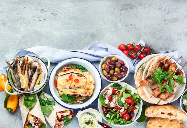 Greek food on grey background. Moussaka, gyros,souvlaki, pita, salad, olives and vegetables. Traditional different types of greek dishes. Top view with copy space
