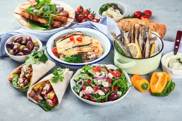 Greek food on grey background. Moussaka, gyros,souvlaki, pita, salad, olives and vegetables. Traditional different types of greek dishes.