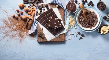 Koyu acı çikolata, kakao yağı, kakao tozu ve mavi arka planda kakao çekirdeği. Çikolata arkaplanı. Kopyalama alanı olan üst görünüm 