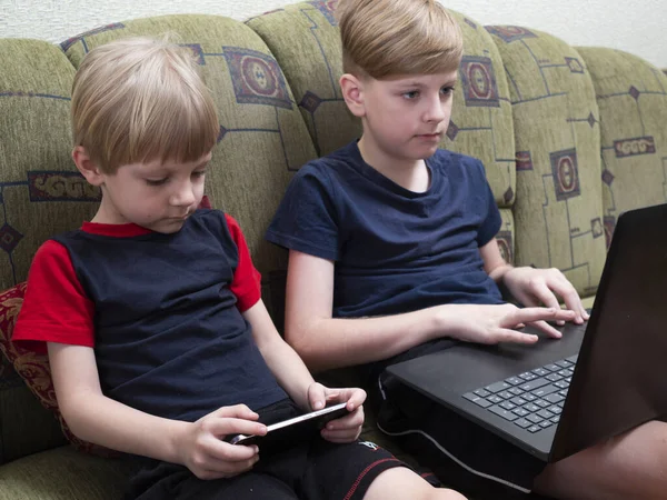 Two schoolboys use internet-connected gadgets for learning, playing games and chatting with friends on social networks, during the coronavirus quarantine.