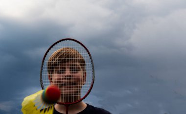 Beyaz çocuk gökyüzünde badminton oynuyor. Çocuk yüzünü bir raketle örttü, bir horoz ona doğru uçtu.
