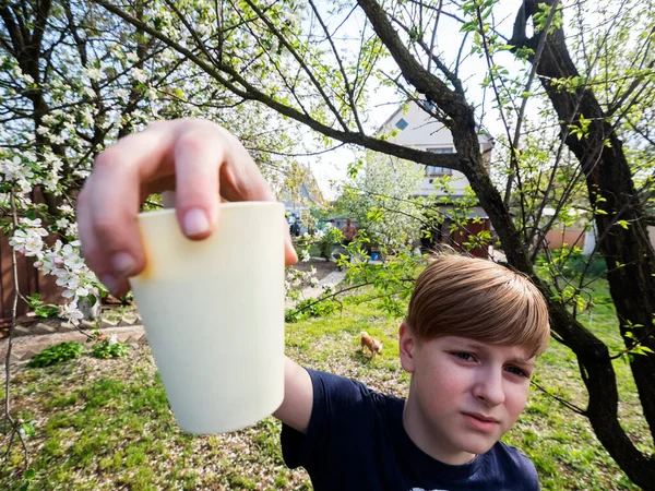 白人の少年は彼の手に花の庭でソフトドリンクとプラスチックガラスを保持しています — ストック写真