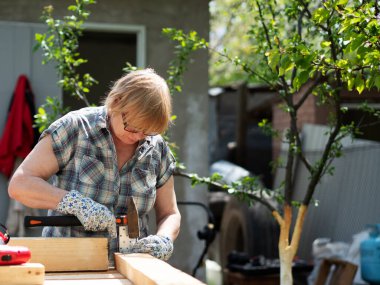 Üst düzey beyaz kadın bir binanın ahşap çerçevesini tornavida kullanarak monte ediyor.