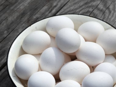 Bahçedeki eski ahşap bir masada metal bir diş minesi kasesinde taze organik tavuk yumurtası.