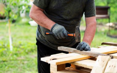 Beyaz bir adamın elleri bahçede bir tahtaya çivi çakıyor.
