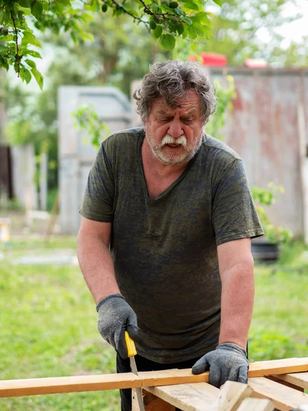 一个成熟的白人男人在花园里锯木松木板 — 图库照片