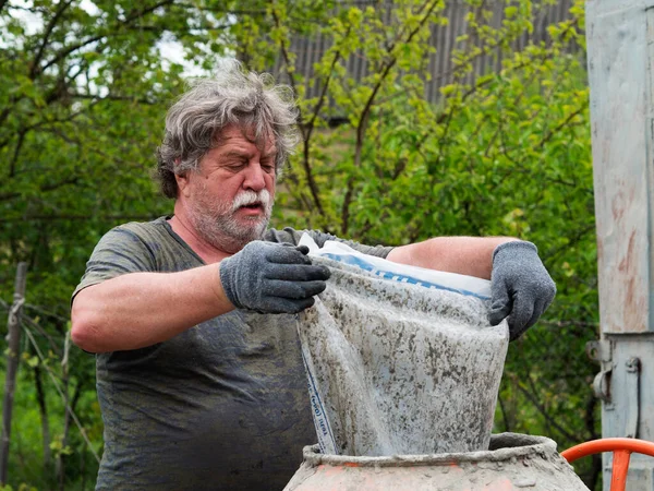 成熟的白人男子把沙砾从袋中倒入混凝土搅拌机 — 图库照片