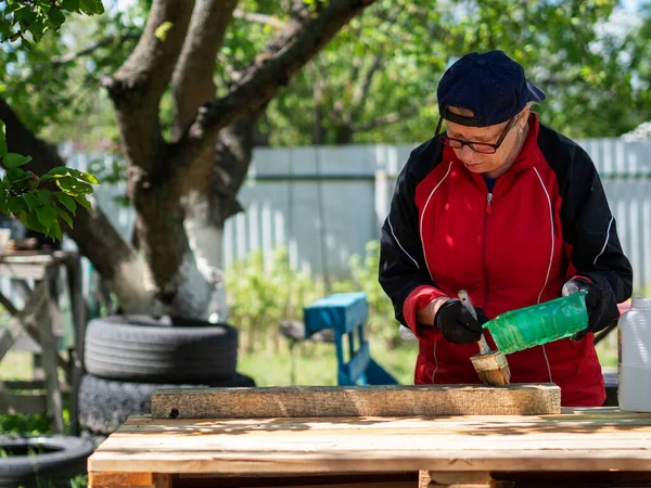 シニア白人女性は腐敗や火災から保護するために防腐剤で木をカバーしています — ストック写真