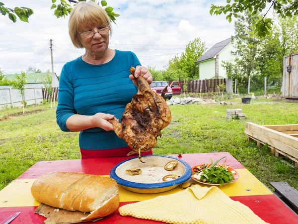 Senior Caucasian woman cuts barbecue chicken
