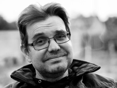 Dost canlısı, tıraşsız, gözlüklü beyaz bir adamın siyah beyaz portresi. 