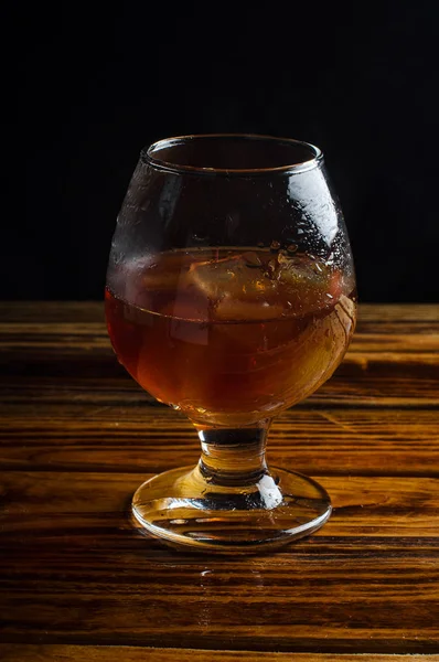 Cognac con ghiaccio in un bicchiere su un tavolo di legno — Foto Stock