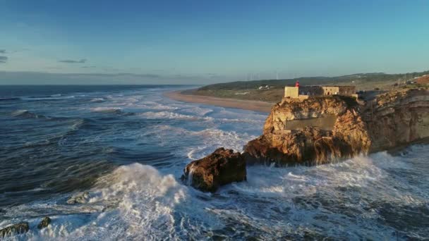 在葡萄牙纳扎尔市 空中俯瞰的是一个悬崖上的灯塔 悬崖上的堡垒位于大西洋沿岸 日落时波涛汹涌 慢动作4K — 图库视频影像