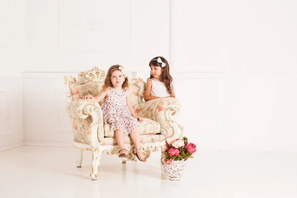 Dos niñas se sienta en un magnífico sillón antiguo — Foto de Stock