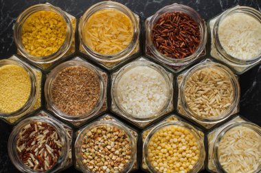 Top view of glass jars with various cereals, rice, couscous, bulgur, and buckwheat.