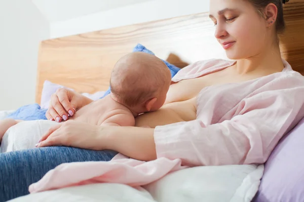 Mujer y niño recién nacido relajarse en un dormitorio blanco . — Foto de Stock