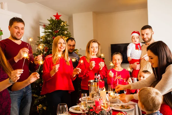 Happy family and friends waiting for Christmas while standing near New Year tree with sparklers in hands. — Stockfoto