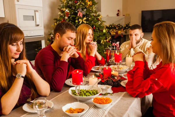 Foto con gruppo di amici che pregano attorno alla tavola di Natale — Foto Stock