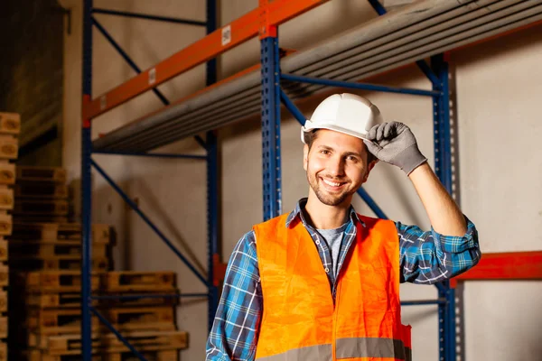 Όμορφος εργάτης με αυτοπεποίθηση με προστατευτικό καπέλο και στολή στην αποθήκη βιομηχανικής παραγωγής — Φωτογραφία Αρχείου