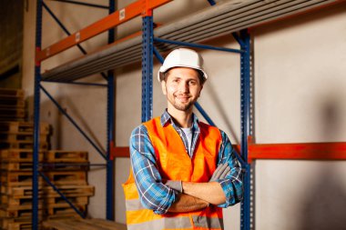 Confident handsome worker in protective hardhat and uniform at the warehouse of a industrial manufacturing