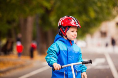 Cute preschooler boy in safety helmet riding a scooter.