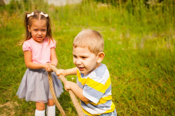 Little friends playing tug of war in a park — ストック写真