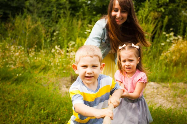 Happy mother and kids playing tug of war in park — ストック写真