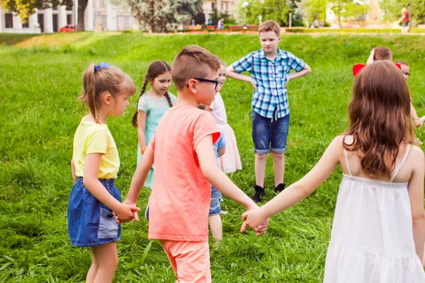 Группа детей, держащихся за руки и танцующих в кругу на зеленой лужайке — стоковое фото