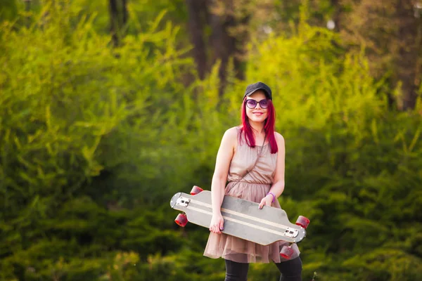 Κομψό αρκετά δροσερό κορίτσι με skateboard πάνω από τη φύση φόντο — Φωτογραφία Αρχείου