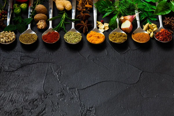 A set of spices and herbs in spoons on black background — Stockfoto