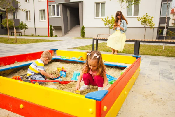 Pequeños niños jugando en la moderna caja de arena con juguetes. Joven familia feliz en un paseo . — Foto de Stock