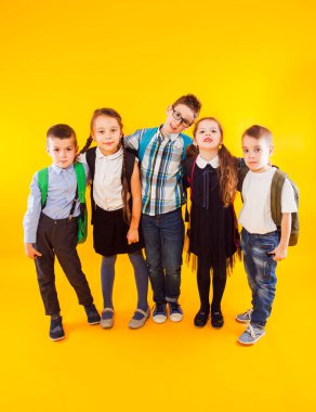 Group of happy school children embracing and standing together in full length on yellow background